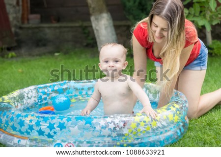 Smiling baby boy playing in inflatable sswimming pool with mother