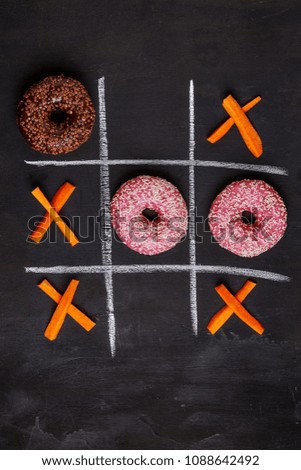 concept idea about junk food and healthy food. tic-tac-toe  carrots and donuts on dark background. top view