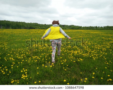 A girl runs in a field of flowers, dandelions. Bright spring picture full of happy and joy.