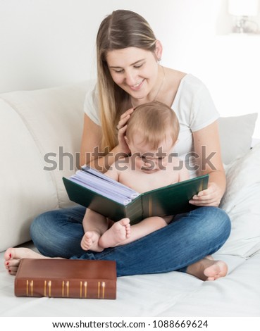 Baby boy sitting on mother lap and watching pictures in big old book
