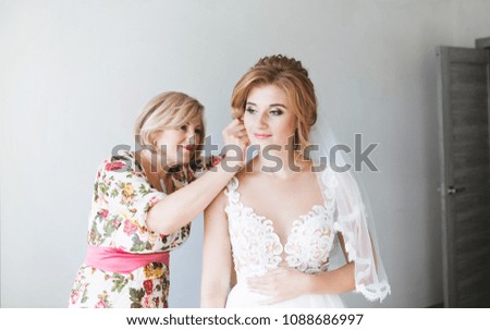 Morning of the bride. Mom helps put on the earrings of a beautiful bride. Mom corrects the wedding hairstyle of the bride. Bride in a beautiful wedding dress. Royalty-Free Stock Photo #1088686997