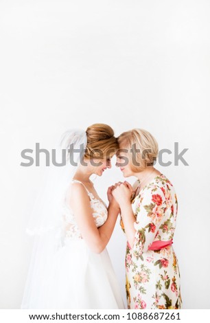Wedding morning of the bride. Mother of the bride blesses the bride for a happy family life. Mom and her daughter joined hands. In the background a bright wall. Royalty-Free Stock Photo #1088687261