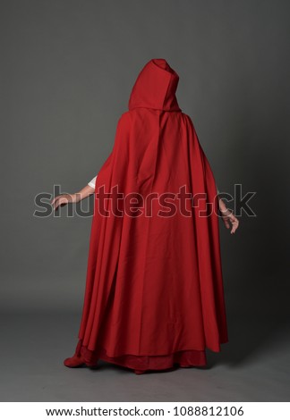 full length portrait of brunette girl wearing red fantasy costume with cloak, standing pose on a guy studio background. Royalty-Free Stock Photo #1088812106