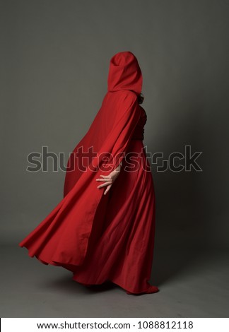 full length portrait of brunette girl wearing red fantasy costume with cloak, standing pose on a guy studio background. Royalty-Free Stock Photo #1088812118