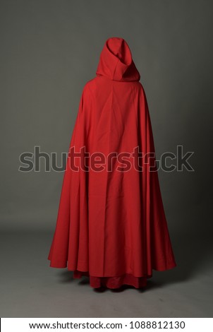 full length portrait of brunette girl wearing red fantasy costume with cloak, standing pose on a guy studio background. Royalty-Free Stock Photo #1088812130