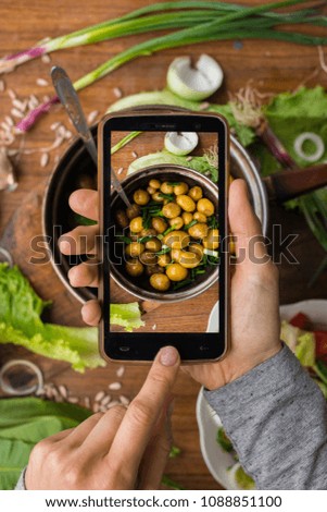 Phone photography of food. Woman hands take photo of lunch with smartphone for social media. Backed new potato in pot. Raw vegan vegetarian healthy dinner 