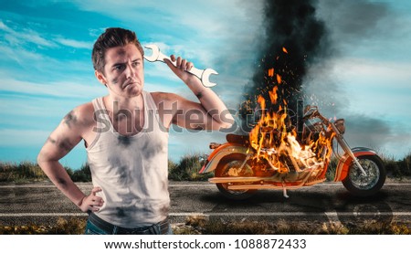 Helpless man holding a wrench with his motorcycle on fire in the background. Needs help to repair the motorbike. 
