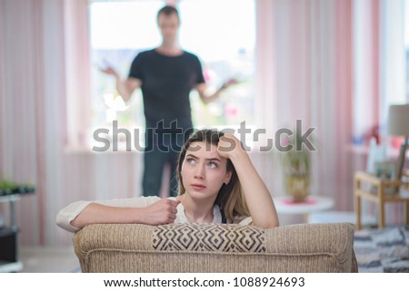 family conflict. Portrait of a teenage girl dissatisfied with talking with her father. She sits right in front of the camera, the father behind in the background is out of focus