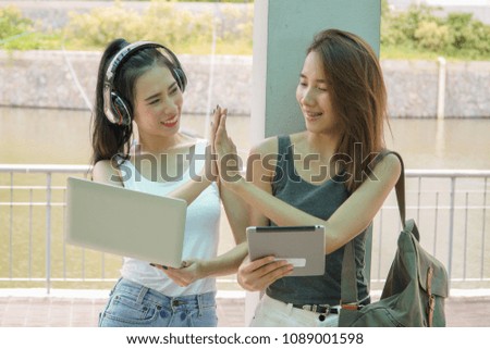 Two Asian women doing high five while using laptop and tablet. Business and technology concept.