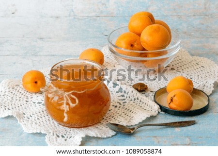 Sweet dessert. A small round jar with homemade jam and fresh ripe apricots on an openwork knitted napkin on an old wooden table. Selective focus.