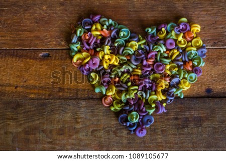 Multicolored pasta in the form of heart on a wooden board. Texture and background.