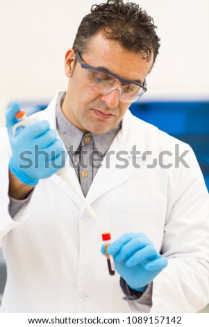 Vertical portrait of a handsome Hispanic mature male scientist working with test tubes and pipette at the laboratory experiment analysis profession concept