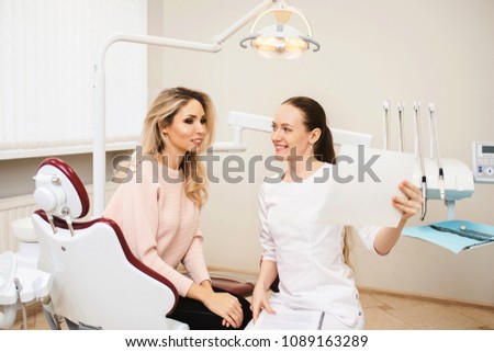 Young female doctor talking with woman patient and showing a radiograph x ray in stomatology clinic. Dentist concept.
