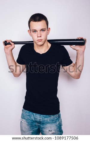 young guy a bully with a short haircut holds a baseball bat in his hands. problematic skin of a teenager: pimples and blackheads. street style in clothes: summer t-shirt and ripped denim shorts