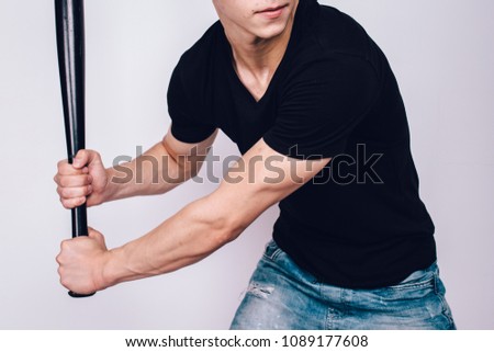 young guy a bully with a short haircut holds a baseball bat in his hands. problematic skin of a teenager: pimples and blackheads. street style in clothes: summer t-shirt and ripped denim shorts