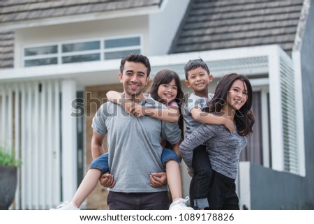 two kids with their parent having fun together in front of their new house. piggyback ride Royalty-Free Stock Photo #1089178826