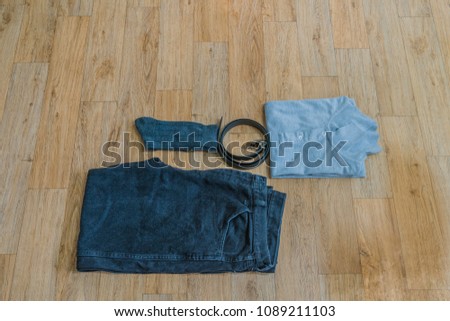 Flat-lay image of black jeans, gray two button pullover, gray crew socks and black belt on wood grain background.