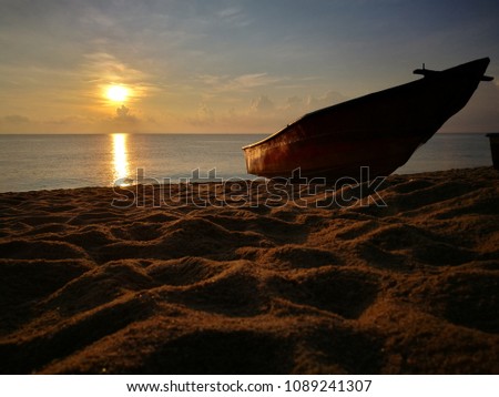 Silhouetted boats at sandy beach during sunrise