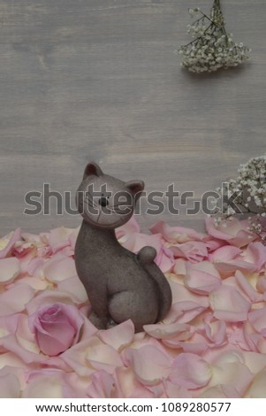 a figure of a cute cat among the petals of a pink rose on a gray background