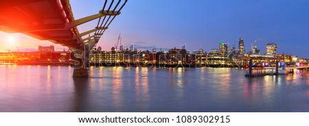 London at sunset, Millennium bridge leading towards illuminated St. Paul cathedral over Thames river with city bathing in electric light. Panoramic toned image. 