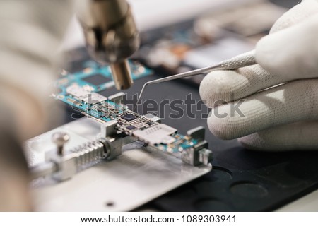 Work with a soldering iron. Microelectronics device. Close-up hands of a service worker repairing modern smartphone. Repair and service concept. Royalty-Free Stock Photo #1089303941