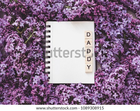 Heart-shaped cookie, covered with bright glaze, word DAD, notepad with a blank page for Your inscription on the background flowers. Top view, close-up. Congratulations for relatives, loved ones