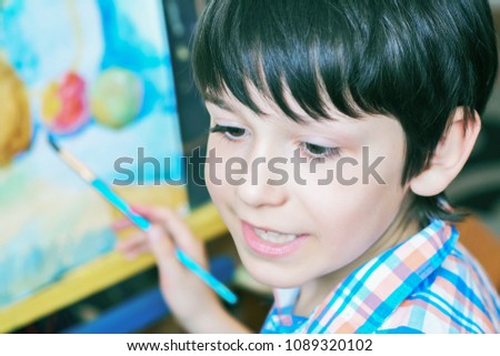 Young boy sitting in front of easel painting a fish, holding a brush in hand. Boy is getting ready to become an artist.