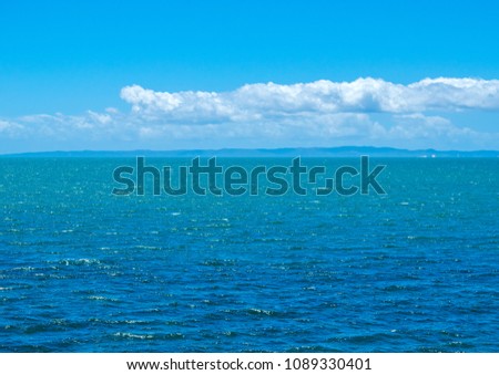 a long distance photo of Moreton Bay Island illuminated by the afternoon sun with a calm ocean and a light blue sky with a passing cloud bank