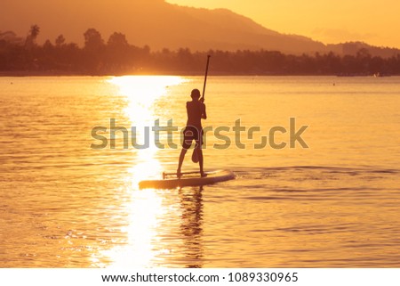 Sunset on the sea, seascape, Silhouette boy Sappsurfing on the background of golden water