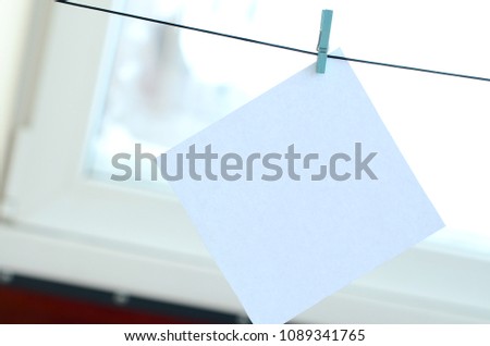 White blank card on rope, window glass background. Creative reminder, small sheet of paper on wooden clothespin, memo backdrop