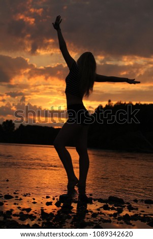 Silhouette of slender young girl with long hair on sunset and river background. Altai territory. Siberia. Russia.