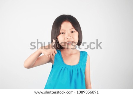 Cute little asian girl giving thumb up hand sign on gray background