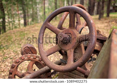 Close-up of an old rusty car steering wheel against a green coniferous forest