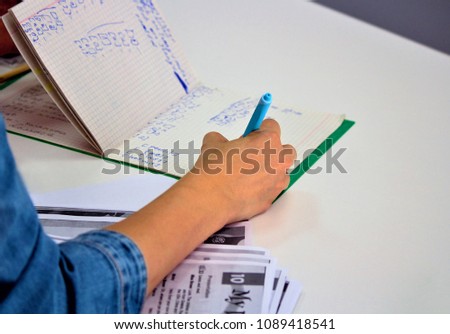 English lesson in the exam room or in the classroom, high school. The teacher holds a pen in his hand, checks the completed task, writes comments.