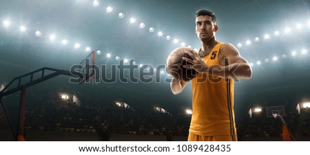 Young muscular basketball player holding a ball on floodlight professional basketbal court
