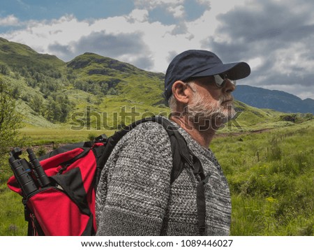 Active senior man standing in valley with red backpack, enjoy looking at mountains landscape.