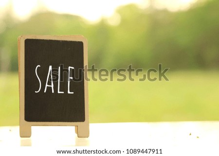 Text Sale in blackboard on top of table with green background.