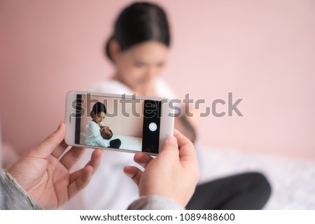 Hand taking pictures on a mobile phone of mother and baby. When the mother is lulling the baby. Pink background.