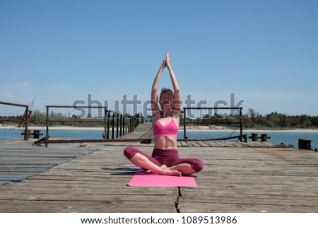 Girl on a pink rug doing yoga at the sea. 