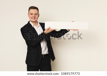 Young successful businessman with blank white banner. Smiling man holding advertising sheet, copy space