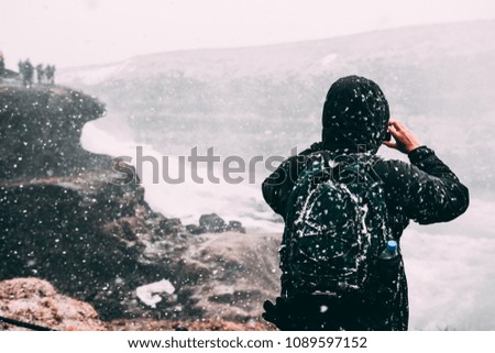 Tourist walking in Iceland in snow storm in famous Golden circle Gullfoss waterfall area, backpacking and taking pictures