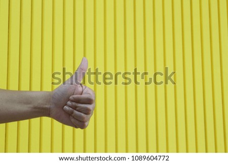A person holding a thumb on a yellow background.