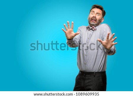 Middle age man, with beard and bow tie disgusted and angry, keeping hands in stop gesture, as a defense, shouting