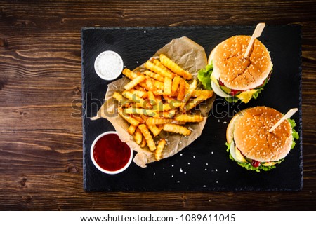 Tasty cheeseburgers with french fries served on fashionable black desk 