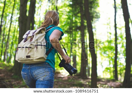 Woman photographer with camera in forest. Travelling girl with backpack climbing on hill. 