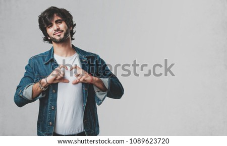 Young handsome man making a heart with hands, expressing the concept of love and friendship, happy and smiling