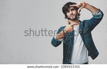 Young handsome man making a frame shape with hands, trying to focus as if it were a camera