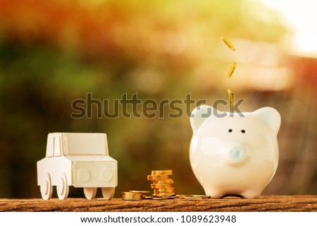 Car model and piggy bank and drop gold coin on the top put on the wood on nature bokeh in the public park, Loan or save money for buy a new chattel concept.