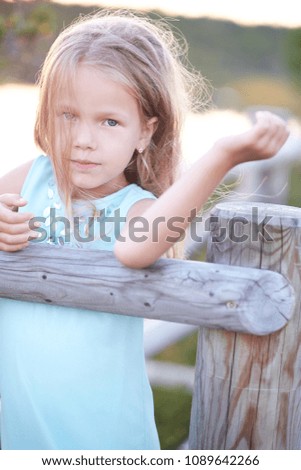 Portrait of a cute little girl, standing outdoors while leaning on a wooden fence.
