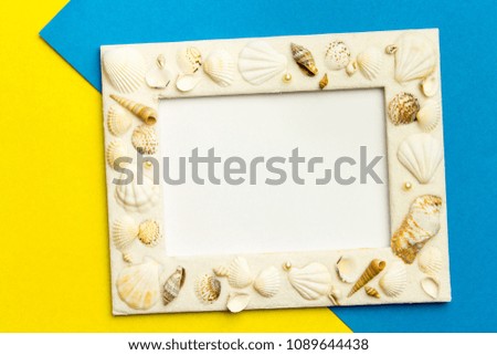 Photo frame with shells on blue and yellow color paper texture background. The concept of a summer vacation.  Summer Flatlay Image